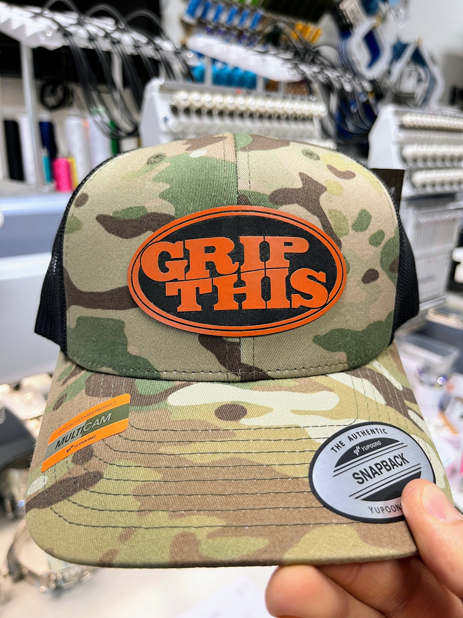 Camouflage Grip This hat with a black and orange custom logo patch