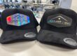 Two all-black suede hats with custom laser-engraved company holographic logo patches
