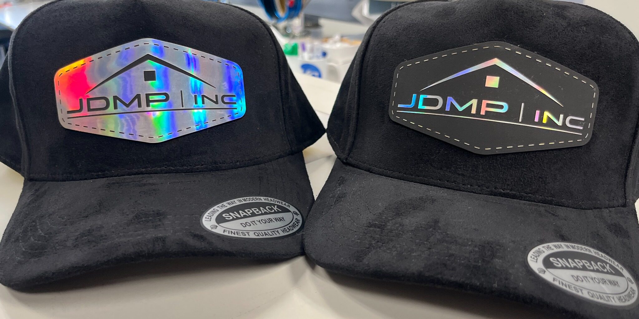 Two all-black suede hats with custom laser-engraved company holographic logo patches Two all-black suede hats with custom laser-engraved company holographic logo patches