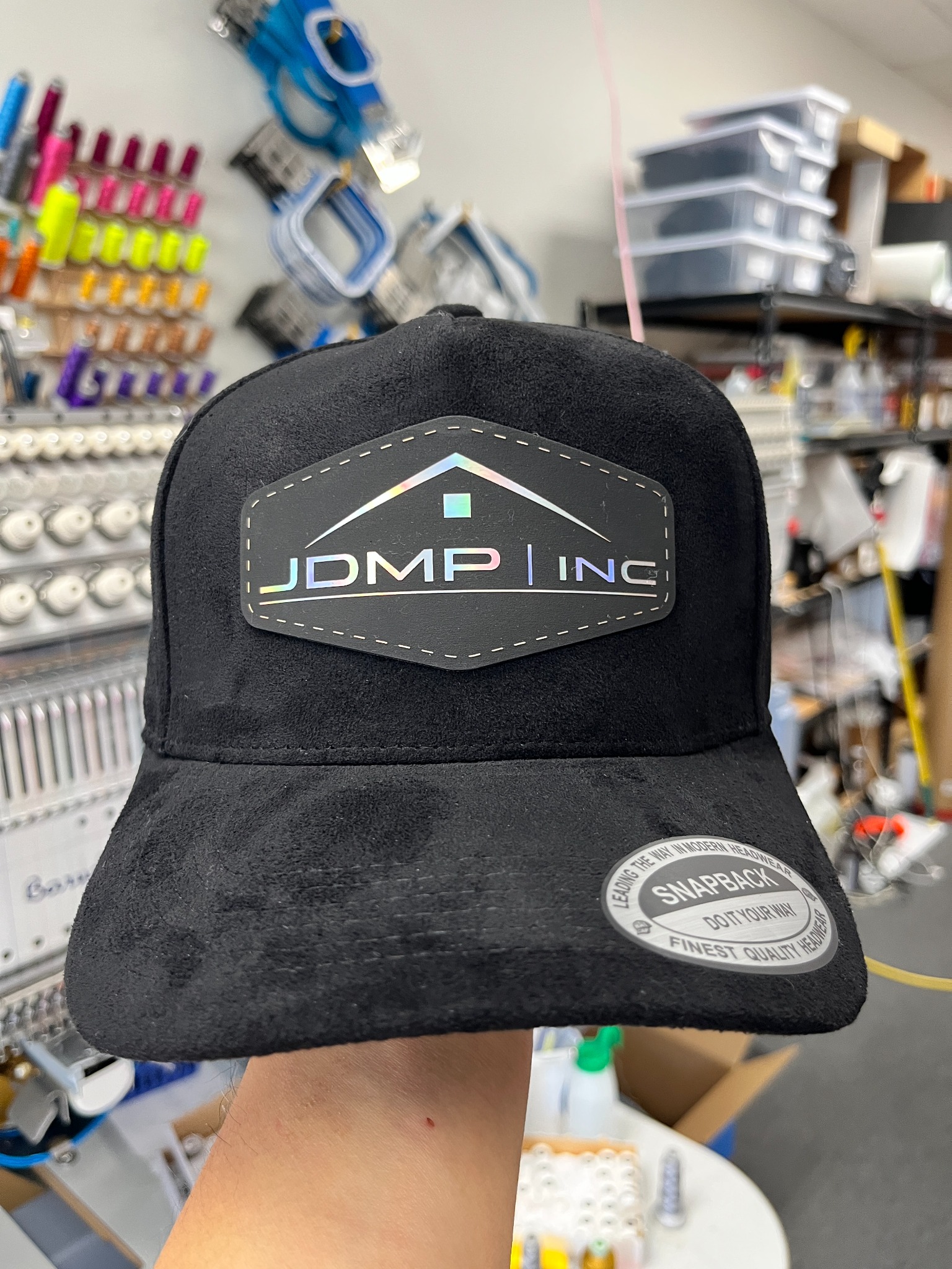 Black suede hat with a shield-shaped company holographic logo patch