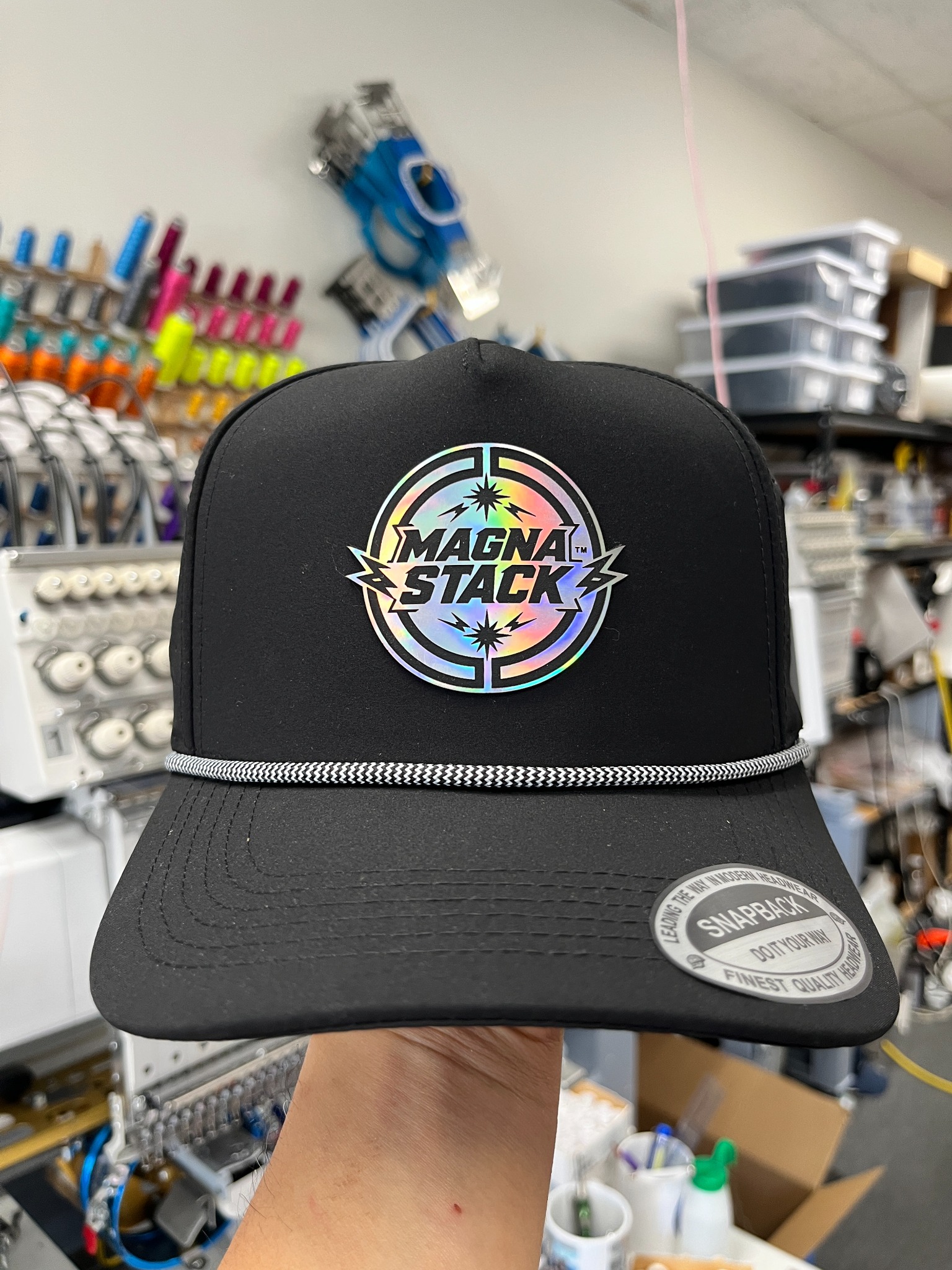 Black five-panel rope hat with a circular Magna Stack holographic logo patch
