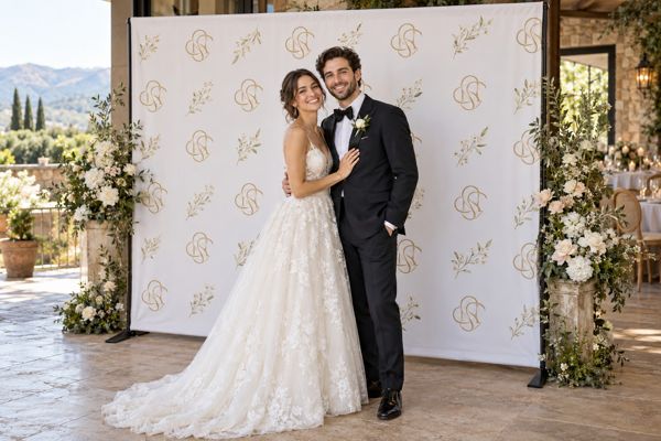 Bride and groom posing in front of a cream and gold wedding backdrop Bride and groom posing in front of a cream and gold wedding backdrop