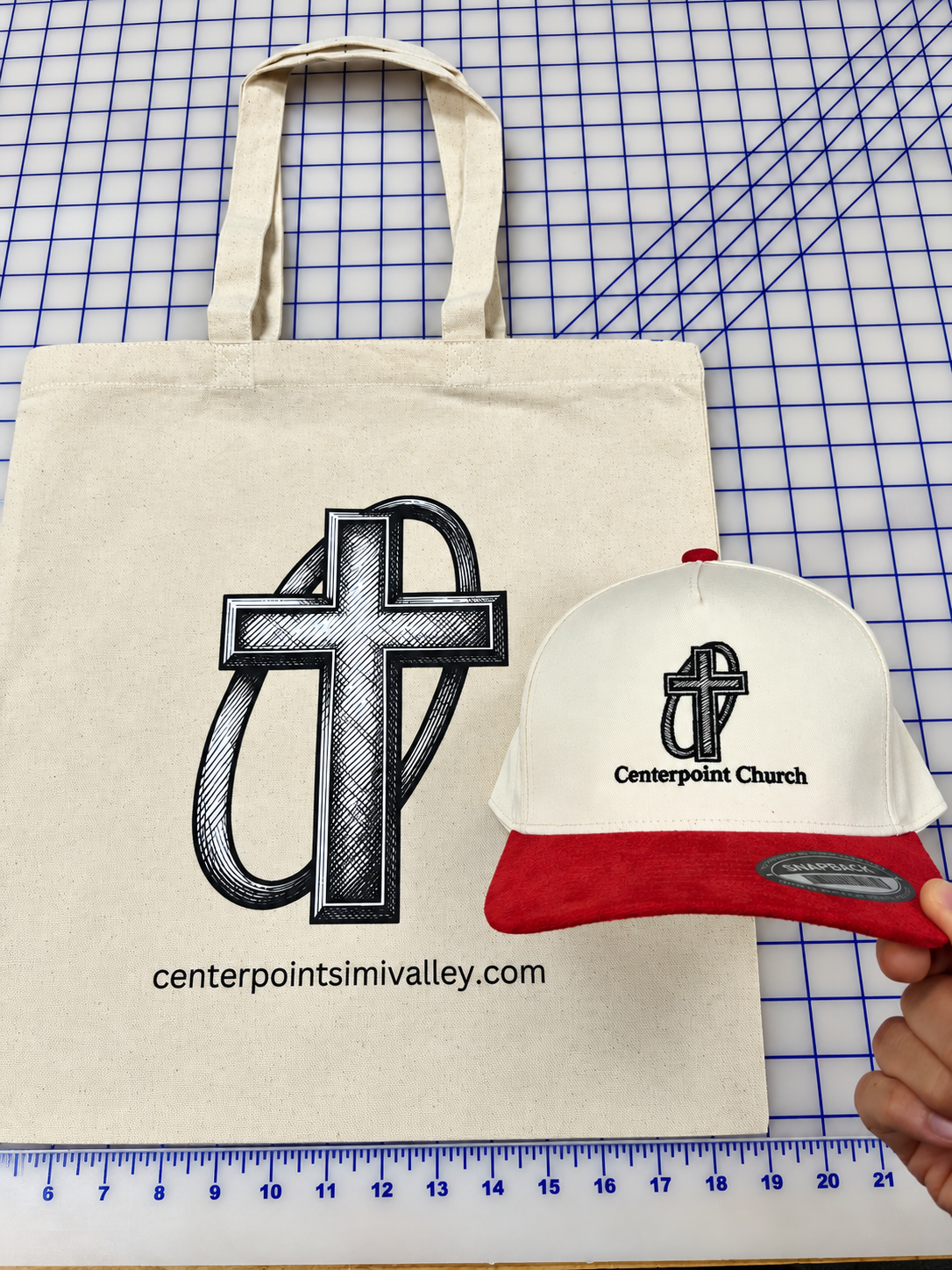 Natural-color Center Point Church tote bag beside a cream and red embroidered hat