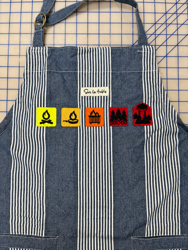 Custom Embroidered Striped Apron | SpectraColor Simi Valley Striped apron with five colorful embroidered fire-themed designs stitched by SpectraColor in Simi Valley.
