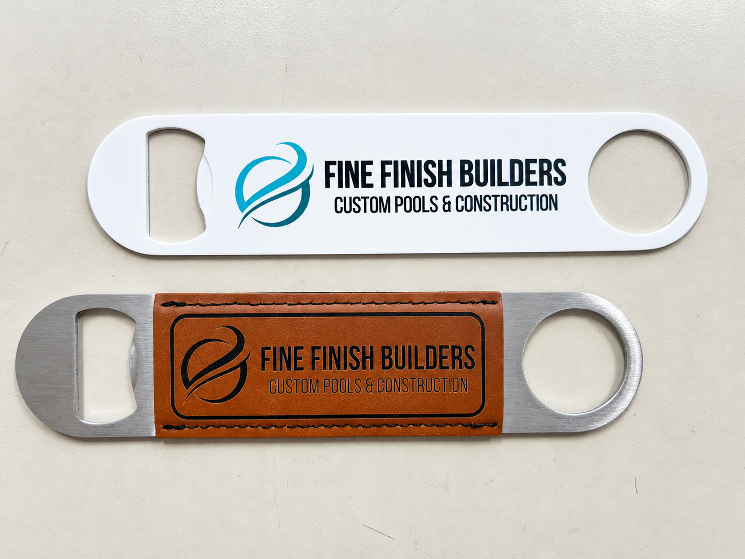 Two Fine Finish Builders branded bottle openers with printed and leather-look logo finishes.
