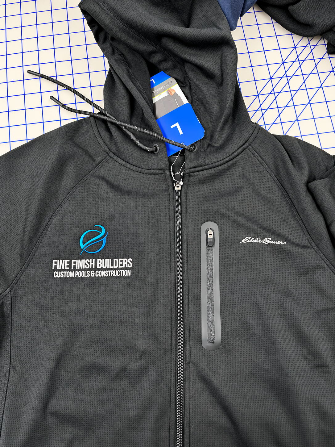 Fine Finish Builders logo embroidered in turquoise and white on a charcoal Eddie Bauer jacket by SpectraColor.