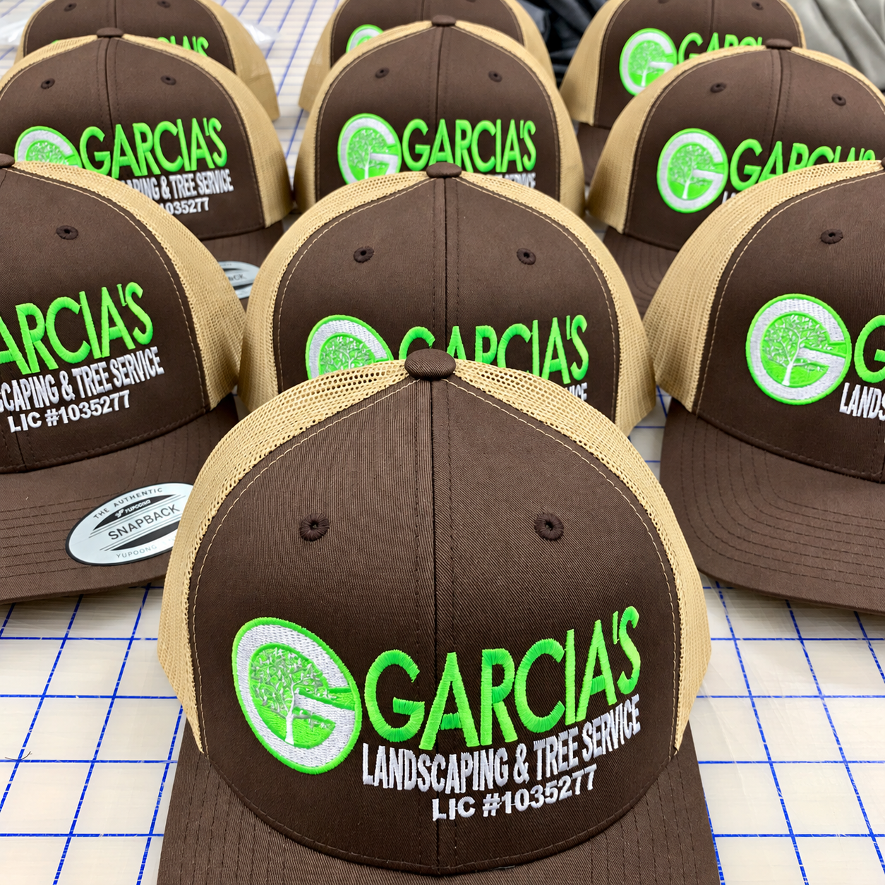 Brown and tan trucker hats embroidered with Garcia’s Landscaping and Tree Service logo in green and white.