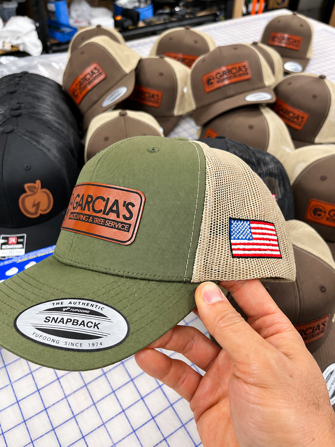 Olive and tan Garcia’s Landscaping leather-patch cap with an embroidered American flag on the side.