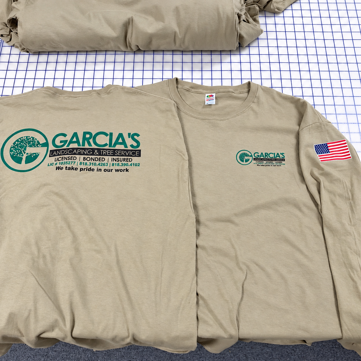 Front and back of tan Garcia’s Landscaping work shirts with green company logo and American flag sleeve print.