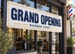 Grand opening vinyl banner hanging by grommets outside a barber shop with a classic barber pole